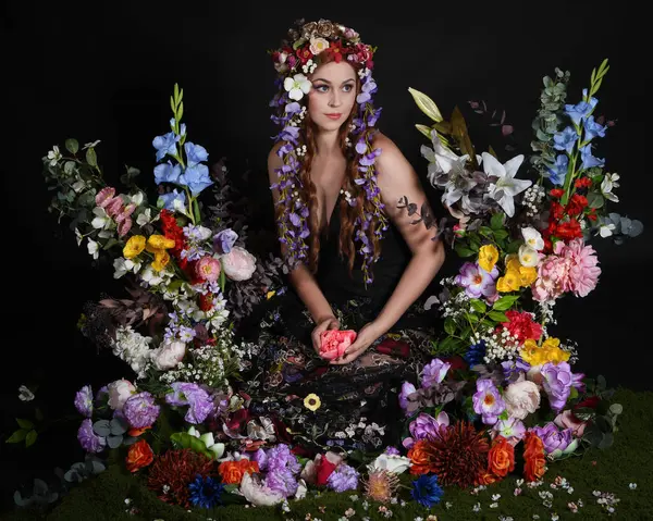 Celtic Bahar Tanrıçası Olarak Kadın Modellerinin Stüdyo Portreleri, Beltane Pagan Mitolojisinden esinlenilmiş Çiçek Peri Fantezi Kostümü. İzole edilmiş Karanlık Stüdyo Arkaplan 'da klasik oturma pozu