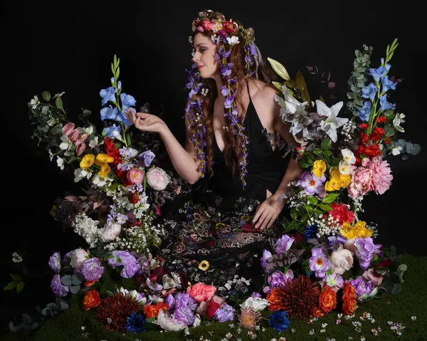 Celtic Bahar Tanrıçası Olarak Kadın Modellerinin Stüdyo Portreleri, Beltane Pagan Mitolojisinden esinlenilmiş Çiçek Peri Fantezi Kostümü. İzole edilmiş Karanlık Stüdyo Arkaplan 'da klasik oturma pozu