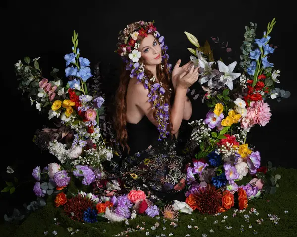 Celtic Bahar Tanrıçası Olarak Kadın Modellerinin Stüdyo Portreleri, Beltane Pagan Mitolojisinden esinlenilmiş Çiçek Peri Fantezi Kostümü. İzole edilmiş Karanlık Stüdyo Arkaplan 'da klasik oturma pozu