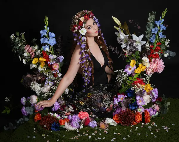 Celtic Bahar Tanrıçası Olarak Kadın Modellerinin Stüdyo Portreleri, Beltane Pagan Mitolojisinden esinlenilmiş Çiçek Peri Fantezi Kostümü. İzole edilmiş Karanlık Stüdyo Arkaplan 'da klasik oturma pozu