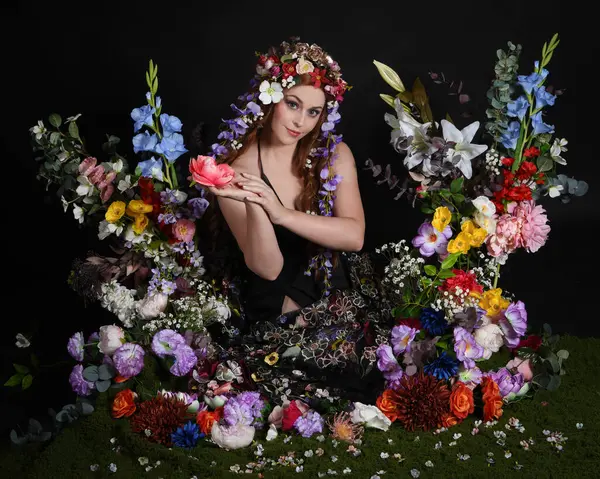 Celtic Bahar Tanrıçası Olarak Kadın Modellerinin Stüdyo Portreleri, Beltane Pagan Mitolojisinden esinlenilmiş Çiçek Peri Fantezi Kostümü. İzole edilmiş Karanlık Stüdyo Arkaplan 'da klasik oturma pozu