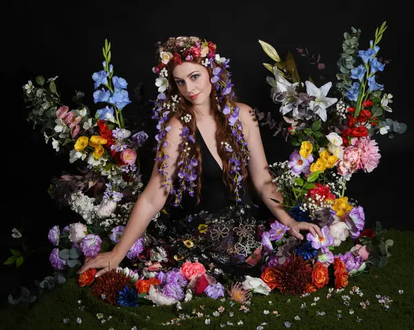 Celtic Bahar Tanrıçası Olarak Kadın Modellerinin Stüdyo Portreleri, Beltane Pagan Mitolojisinden esinlenilmiş Çiçek Peri Fantezi Kostümü. İzole edilmiş Karanlık Stüdyo Arkaplan 'da klasik oturma pozu