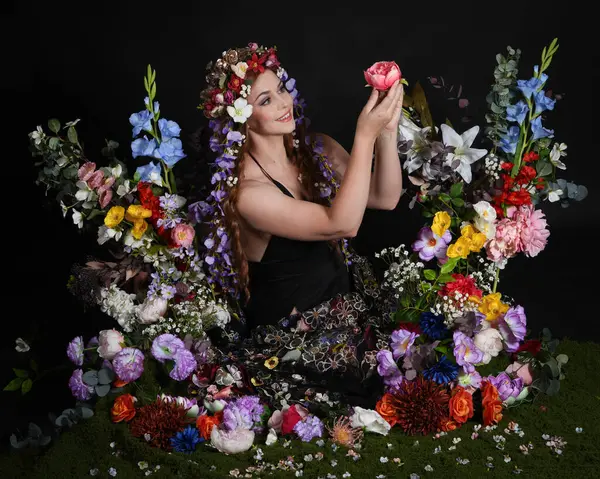 Celtic Bahar Tanrıçası Olarak Kadın Modellerinin Stüdyo Portreleri, Beltane Pagan Mitolojisinden esinlenilmiş Çiçek Peri Fantezi Kostümü. İzole edilmiş Karanlık Stüdyo Arkaplan 'da klasik oturma pozu