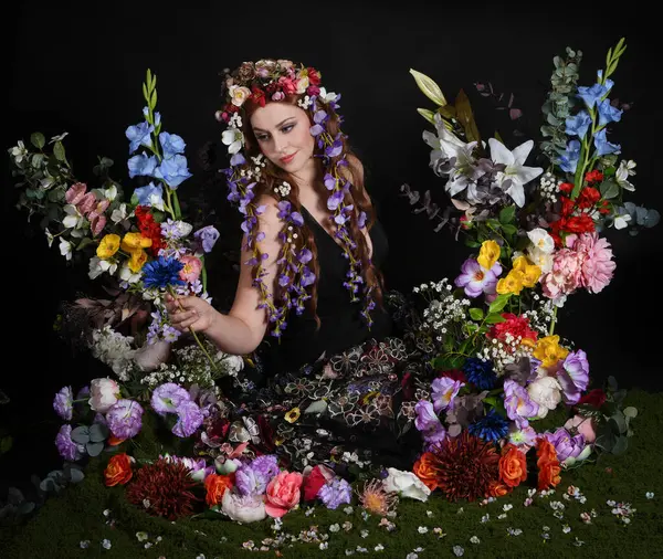 Celtic Bahar Tanrıçası Olarak Kadın Modellerinin Stüdyo Portreleri, Beltane Pagan Mitolojisinden esinlenilmiş Çiçek Peri Fantezi Kostümü. İzole edilmiş Karanlık Stüdyo Arkaplan 'da klasik oturma pozu