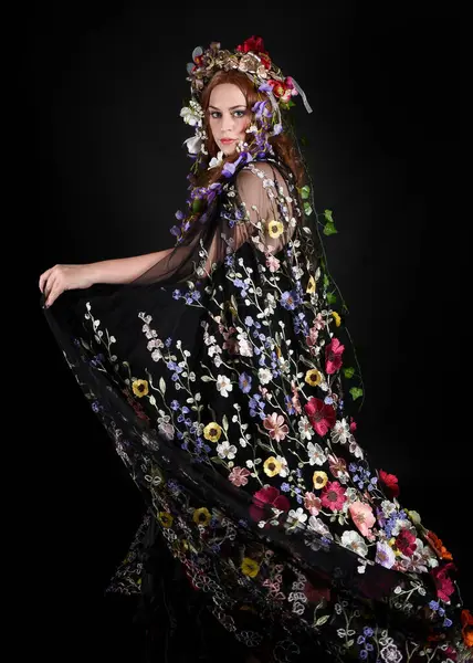 Celtic Bahar Tanrıçası Olarak Kadın Model Stüdyo Portreleri, Beltane Pagan Mitolojisinden esinlenerek Çiçek Fantezi Pelerini Kostümü. Kol hareketleriyle klasik poz, izole edilmiş Karanlık Arkaplan