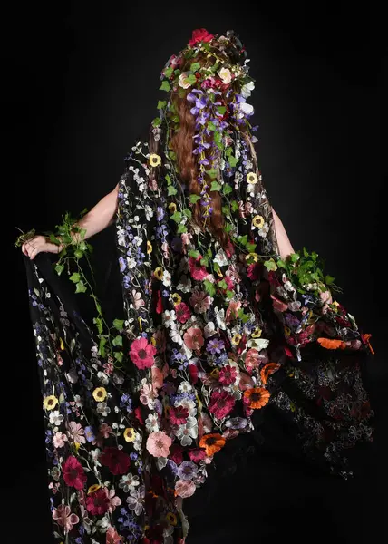 Celtic Bahar Tanrıçası Olarak Kadın Model Stüdyo Portreleri, Beltane Pagan Mitolojisinden esinlenerek Çiçek Fantezi Pelerini Kostümü. Kol hareketleriyle klasik poz, izole edilmiş Karanlık Arkaplan