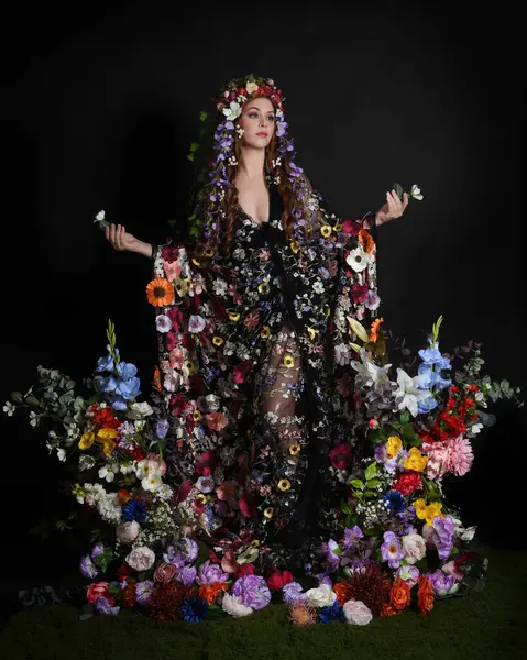 Celtic Bahar Tanrıçası Olarak Kadın Model Stüdyo Portreleri, Beltane Pagan Mitolojisinden esinlenerek Çiçek Fantezi Pelerini Kostümü. Kol hareketleriyle klasik poz, izole edilmiş Karanlık Arkaplan