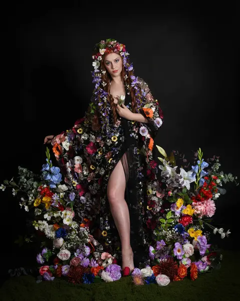 Celtic Bahar Tanrıçası Olarak Kadın Modellerinin Stüdyo Portreleri, Beltane Pagan Mitolojisinden esinlenilmiş Çiçek Peri Fantezi Kostümü. İzole edilmiş Karanlık Stüdyo Arkaplanda Pelerinli Klasik Duruş