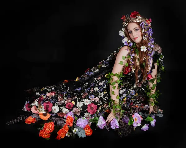 Celtic Bahar Tanrıçası Olarak Kadın Model Stüdyo Portreleri, Beltane Pagan Mitolojisinden esinlenerek Çiçek Fantezi Pelerini Kostümü. Klasik oturma pozisyonu, kollar uzanıyor. izole edilmiş Karanlık Arkaplan