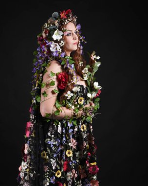 Kelt Bahar Tanrıçası Olarak Güzel Kadın Modeli Portreleri, Beltane Pagan Mitolojisinden esinlenerek Çiçek Fantezi Pelerini Kostümü. izole Karanlık Stüdyo Arkaplanı