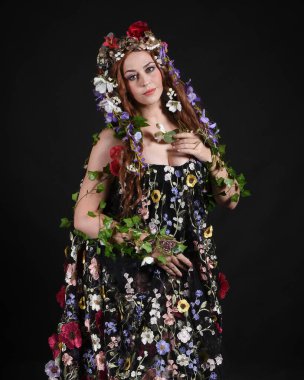 Kelt Bahar Tanrıçası Olarak Güzel Kadın Modeli Portreleri, Beltane Pagan Mitolojisinden esinlenerek Çiçek Fantezi Pelerini Kostümü. izole Karanlık Stüdyo Arkaplanı