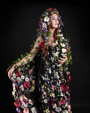 Kelt Bahar Tanrıçası Olarak Güzel Kadın Modeli Portreleri, Beltane Pagan Mitolojisinden esinlenerek Çiçek Fantezi Pelerini Kostümü. izole Karanlık Stüdyo Arkaplanı