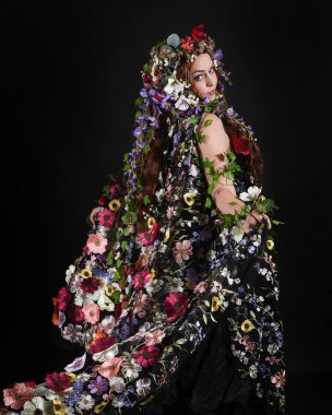 Kelt Bahar Tanrıçası Olarak Güzel Kadın Modeli Portreleri, Beltane Pagan Mitolojisinden esinlenerek Çiçek Fantezi Pelerini Kostümü. izole Karanlık Stüdyo Arkaplanı