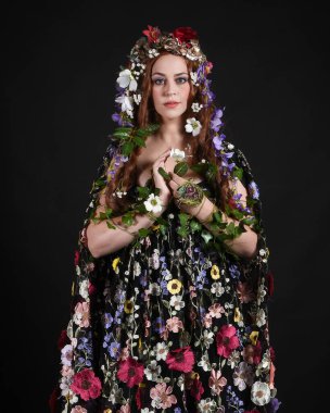 Kelt Bahar Tanrıçası Olarak Güzel Kadın Modeli Portreleri, Beltane Pagan Mitolojisinden esinlenerek Çiçek Fantezi Pelerini Kostümü. izole Karanlık Stüdyo Arkaplanı