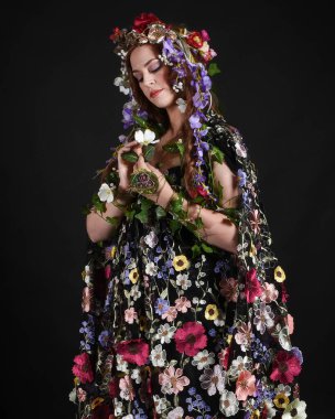 Kelt Bahar Tanrıçası Olarak Güzel Kadın Modeli Portreleri, Beltane Pagan Mitolojisinden esinlenerek Çiçek Fantezi Pelerini Kostümü. izole Karanlık Stüdyo Arkaplanı
