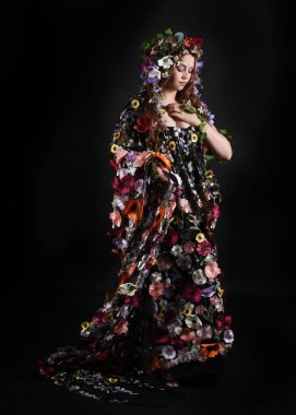 Kelt Bahar Tanrıçası Olarak Kadın Modeli 'nin Portresi Beltane Pagan Mitolojisinden esinlenerek Çiçek Fantezi Pelerini Kostümü. Uzaklaşmak, geriye doğru poz vermek, Karanlık Stüdyo Arkaplanı 'nda soyutlanmak