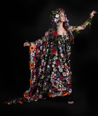 Kelt Bahar Tanrıçası Olarak Kadın Modeli 'nin Portresi Beltane Pagan Mitolojisinden esinlenerek Çiçek Fantezi Pelerini Kostümü. Uzaklaşmak, geriye doğru poz vermek, Karanlık Stüdyo Arkaplanı 'nda soyutlanmak