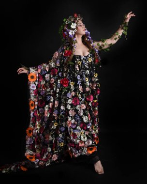 Kelt Bahar Tanrıçası Olarak Kadın Modeli 'nin Portresi Beltane Pagan Mitolojisinden esinlenerek Çiçek Fantezi Pelerini Kostümü. Uzaklaşmak, geriye doğru poz vermek, Karanlık Stüdyo Arkaplanı 'nda soyutlanmak