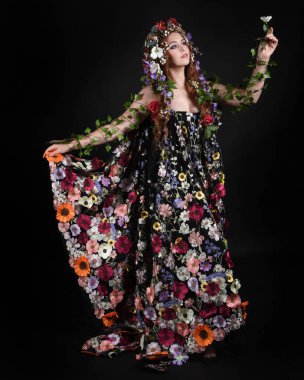 Kelt Bahar Tanrıçası Olarak Kadın Modeli 'nin Portresi Beltane Pagan Mitolojisinden esinlenerek Çiçek Fantezi Pelerini Kostümü. Uzaklaşmak, geriye doğru poz vermek, Karanlık Stüdyo Arkaplanı 'nda soyutlanmak