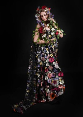 Kelt Bahar Tanrıçası Olarak Kadın Modeli 'nin Portresi Beltane Pagan Mitolojisinden esinlenerek Çiçek Fantezi Pelerini Kostümü. Uzaklaşmak, geriye doğru poz vermek, Karanlık Stüdyo Arkaplanı 'nda soyutlanmak