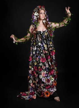 Kelt Bahar Tanrıçası Olarak Kadın Modeli 'nin Portresi Beltane Pagan Mitolojisinden esinlenerek Çiçek Fantezi Pelerini Kostümü. Uzaklaşmak, geriye doğru poz vermek, Karanlık Stüdyo Arkaplanı 'nda soyutlanmak