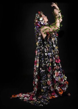 Kelt Bahar Tanrıçası Olarak Kadın Modeli 'nin Portresi Beltane Pagan Mitolojisinden esinlenerek Çiçek Fantezi Pelerini Kostümü. Uzaklaşmak, geriye doğru poz vermek, Karanlık Stüdyo Arkaplanı 'nda soyutlanmak