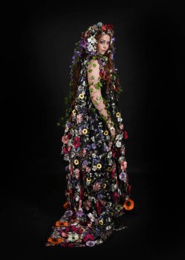 Kelt Bahar Tanrıçası Olarak Kadın Modeli 'nin Portresi Beltane Pagan Mitolojisinden esinlenerek Çiçek Fantezi Pelerini Kostümü. Uzaklaşmak, geriye doğru poz vermek, Karanlık Stüdyo Arkaplanı 'nda soyutlanmak