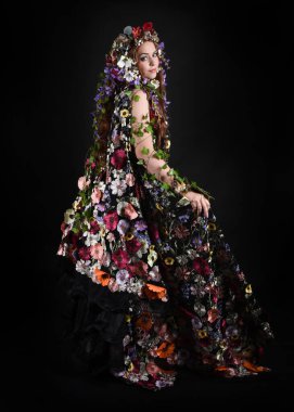 Kelt Bahar Tanrıçası Olarak Kadın Modeli 'nin Portresi Beltane Pagan Mitolojisinden esinlenerek Çiçek Fantezi Pelerini Kostümü. Uzaklaşmak, geriye doğru poz vermek, Karanlık Stüdyo Arkaplanı 'nda soyutlanmak
