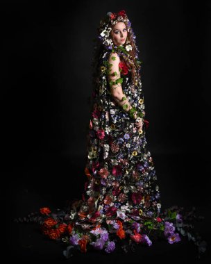 Kelt Bahar Tanrıçası Olarak Kadın Modeli 'nin Portresi Beltane Pagan Mitolojisinden esinlenerek Çiçek Fantezi Pelerini Kostümü. Uzaklaşmak, geriye doğru poz vermek, Karanlık Stüdyo Arkaplanı 'nda soyutlanmak
