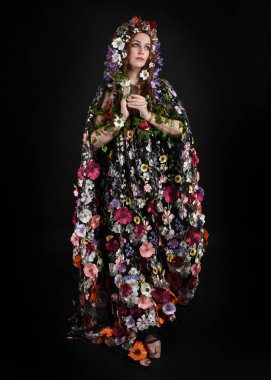 Kelt Bahar Tanrıçası Olarak Kadın Modeli 'nin Portresi Beltane Pagan Mitolojisinden esinlenerek Çiçek Fantezi Pelerini Kostümü. Uzaklaşmak, geriye doğru poz vermek, Karanlık Stüdyo Arkaplanı 'nda soyutlanmak
