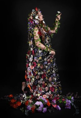 Kelt Bahar Tanrıçası Olarak Kadın Modeli 'nin Portresi Beltane Pagan Mitolojisinden esinlenerek Çiçek Fantezi Pelerini Kostümü. Uzaklaşmak, geriye doğru poz vermek, Karanlık Stüdyo Arkaplanı 'nda soyutlanmak
