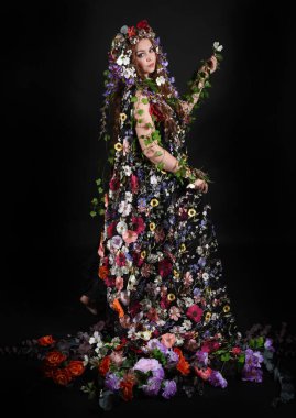 Kelt Bahar Tanrıçası Olarak Kadın Modeli 'nin Portresi Beltane Pagan Mitolojisinden esinlenerek Çiçek Fantezi Pelerini Kostümü. Uzaklaşmak, geriye doğru poz vermek, Karanlık Stüdyo Arkaplanı 'nda soyutlanmak