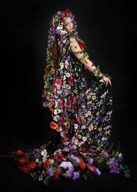 Kelt Bahar Tanrıçası Olarak Kadın Modeli 'nin Portresi Beltane Pagan Mitolojisinden esinlenerek Çiçek Fantezi Pelerini Kostümü. Uzaklaşmak, geriye doğru poz vermek, Karanlık Stüdyo Arkaplanı 'nda soyutlanmak