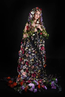 Kelt Bahar Tanrıçası Olarak Kadın Modeli 'nin Portresi Beltane Pagan Mitolojisinden esinlenerek Çiçek Fantezi Pelerini Kostümü. Uzaklaşmak, geriye doğru poz vermek, Karanlık Stüdyo Arkaplanı 'nda soyutlanmak