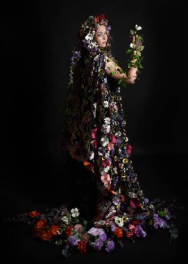 Kelt Bahar Tanrıçası Olarak Kadın Modeli 'nin Portresi Beltane Pagan Mitolojisinden esinlenerek Çiçek Fantezi Pelerini Kostümü. Uzaklaşmak, geriye doğru poz vermek, Karanlık Stüdyo Arkaplanı 'nda soyutlanmak