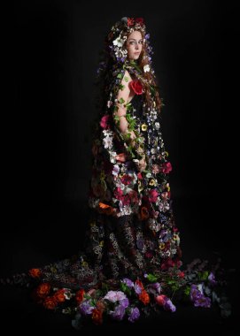 Kelt Bahar Tanrıçası Olarak Kadın Modeli 'nin Portresi Beltane Pagan Mitolojisinden esinlenerek Çiçek Fantezi Pelerini Kostümü. Uzaklaşmak, geriye doğru poz vermek, Karanlık Stüdyo Arkaplanı 'nda soyutlanmak