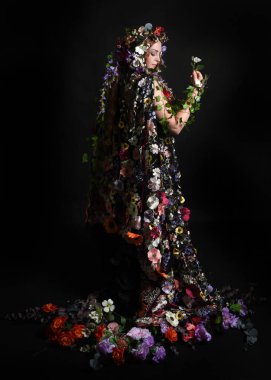 Kelt Bahar Tanrıçası Olarak Kadın Modeli 'nin Portresi Beltane Pagan Mitolojisinden esinlenerek Çiçek Fantezi Pelerini Kostümü. Uzaklaşmak, geriye doğru poz vermek, Karanlık Stüdyo Arkaplanı 'nda soyutlanmak