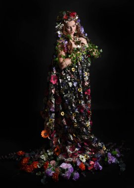 Kelt Bahar Tanrıçası Olarak Kadın Modeli 'nin Portresi Beltane Pagan Mitolojisinden esinlenerek Çiçek Fantezi Pelerini Kostümü. Uzaklaşmak, geriye doğru poz vermek, Karanlık Stüdyo Arkaplanı 'nda soyutlanmak