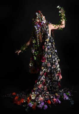Kelt Bahar Tanrıçası Olarak Kadın Modeli 'nin Portresi Beltane Pagan Mitolojisinden esinlenerek Çiçek Fantezi Pelerini Kostümü. Uzaklaşmak, geriye doğru poz vermek, Karanlık Stüdyo Arkaplanı 'nda soyutlanmak