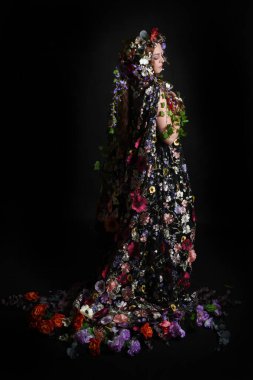 Kelt Bahar Tanrıçası Olarak Kadın Modeli 'nin Portresi Beltane Pagan Mitolojisinden esinlenerek Çiçek Fantezi Pelerini Kostümü. Uzaklaşmak, geriye doğru poz vermek, Karanlık Stüdyo Arkaplanı 'nda soyutlanmak