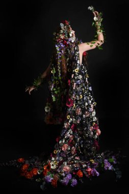 Kelt Bahar Tanrıçası Olarak Kadın Modeli 'nin Portresi Beltane Pagan Mitolojisinden esinlenerek Çiçek Fantezi Pelerini Kostümü. Uzaklaşmak, geriye doğru poz vermek, Karanlık Stüdyo Arkaplanı 'nda soyutlanmak