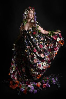 Kelt Bahar Tanrıçası Olarak Kadın Modeli 'nin Portresi Beltane Pagan Mitolojisinden esinlenerek Çiçek Fantezi Pelerini Kostümü. Uzaklaşmak, geriye doğru poz vermek, Karanlık Stüdyo Arkaplanı 'nda soyutlanmak