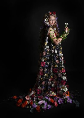 Kelt Bahar Tanrıçası Olarak Kadın Modeli 'nin Portresi Beltane Pagan Mitolojisinden esinlenerek Çiçek Fantezi Pelerini Kostümü. Uzaklaşmak, geriye doğru poz vermek, Karanlık Stüdyo Arkaplanı 'nda soyutlanmak