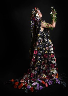 Kelt Bahar Tanrıçası Olarak Kadın Modeli 'nin Portresi Beltane Pagan Mitolojisinden esinlenerek Çiçek Fantezi Pelerini Kostümü. Uzaklaşmak, geriye doğru poz vermek, Karanlık Stüdyo Arkaplanı 'nda soyutlanmak