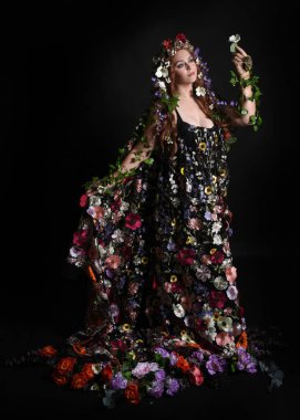 Kelt Bahar Tanrıçası Olarak Kadın Modeli 'nin Portresi Beltane Pagan Mitolojisinden esinlenerek Çiçek Fantezi Pelerini Kostümü. Uzaklaşmak, geriye doğru poz vermek, Karanlık Stüdyo Arkaplanı 'nda soyutlanmak
