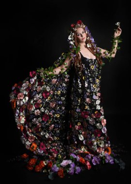Kelt Bahar Tanrıçası Olarak Kadın Modeli 'nin Portresi Beltane Pagan Mitolojisinden esinlenerek Çiçek Fantezi Pelerini Kostümü. Uzaklaşmak, geriye doğru poz vermek, Karanlık Stüdyo Arkaplanı 'nda soyutlanmak