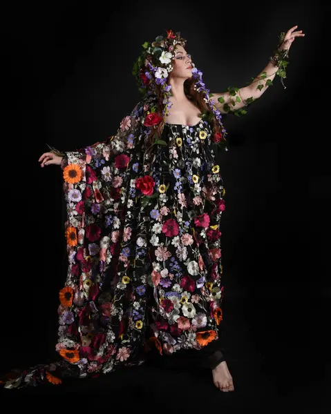 Kelt Bahar Tanrıçası Olarak Kadın Modeli 'nin Portresi Beltane Pagan Mitolojisinden esinlenerek Çiçek Fantezi Pelerini Kostümü. Uzaklaşmak, geriye doğru poz vermek, Karanlık Stüdyo Arkaplanı 'nda soyutlanmak