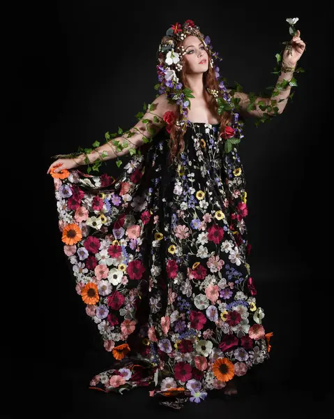 Kelt Bahar Tanrıçası Olarak Kadın Modeli 'nin Portresi Beltane Pagan Mitolojisinden esinlenerek Çiçek Fantezi Pelerini Kostümü. Uzaklaşmak, geriye doğru poz vermek, Karanlık Stüdyo Arkaplanı 'nda soyutlanmak