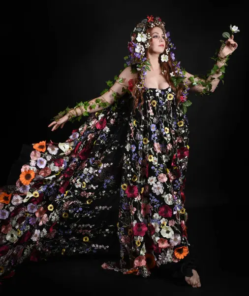 Kelt Bahar Tanrıçası Olarak Kadın Modeli 'nin Portresi Beltane Pagan Mitolojisinden esinlenerek Çiçek Fantezi Pelerini Kostümü. Uzaklaşmak, geriye doğru poz vermek, Karanlık Stüdyo Arkaplanı 'nda soyutlanmak