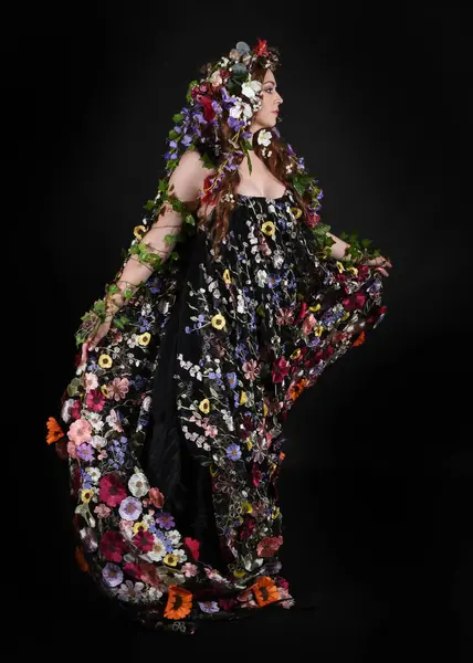 Kelt Bahar Tanrıçası Olarak Kadın Modeli 'nin Portresi Beltane Pagan Mitolojisinden esinlenerek Çiçek Fantezi Pelerini Kostümü. Uzaklaşmak, geriye doğru poz vermek, Karanlık Stüdyo Arkaplanı 'nda soyutlanmak